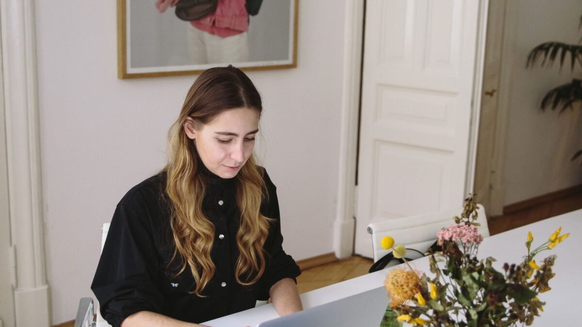 Mujer trabajando con una laptop en un escritorio con documentos y flores