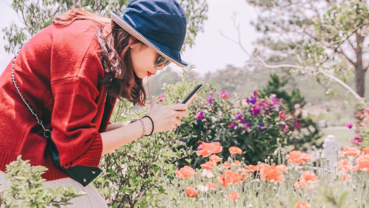 Mujer fotografiando flores con su celular en un jardín soleado