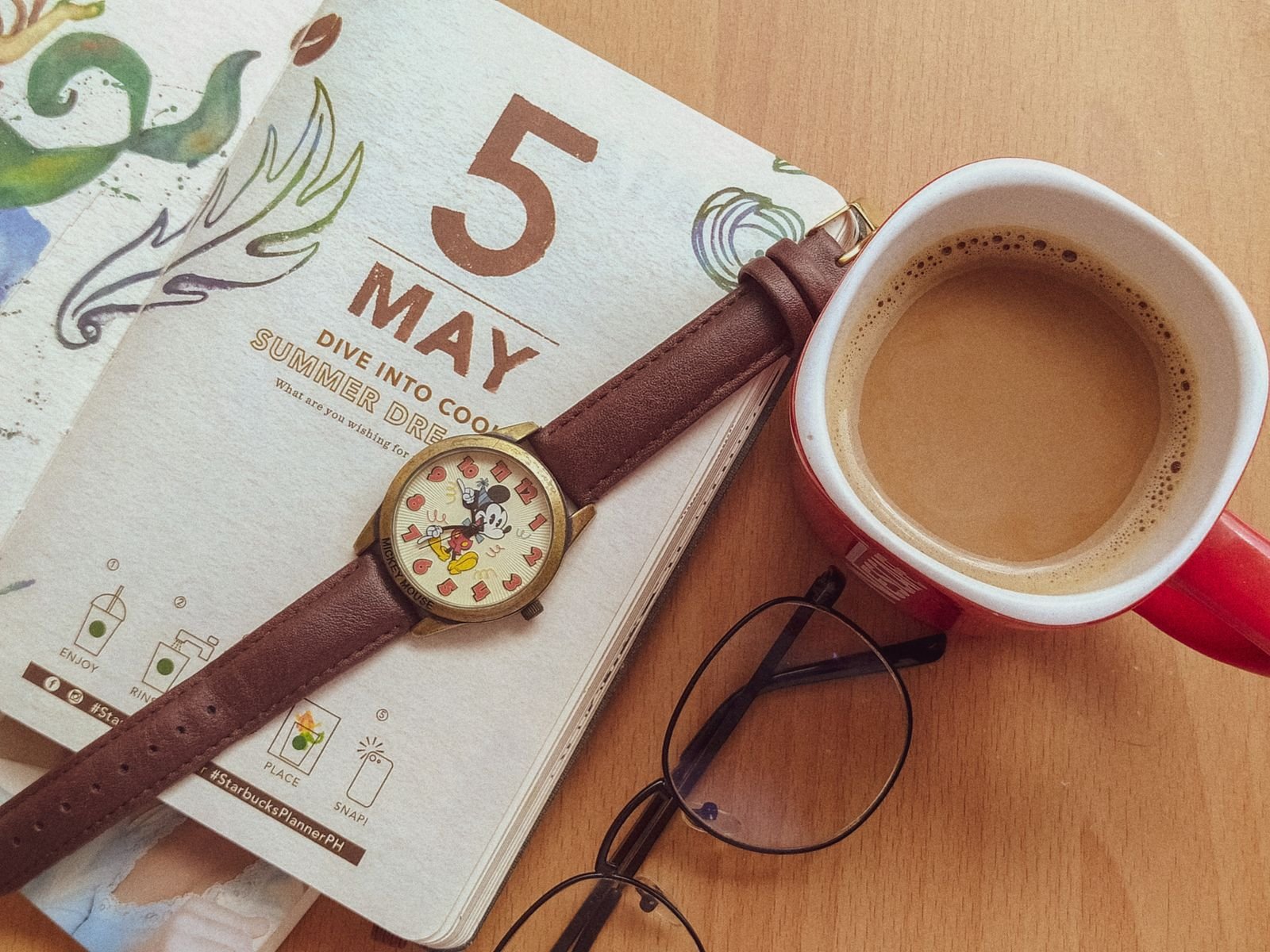 Escritorio de freelancer visto desde arriba con agenda, café, reloj y lentes