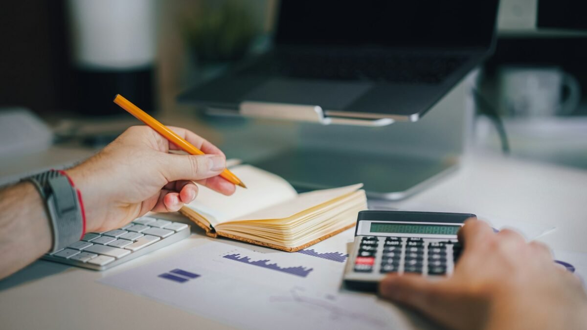Persona sentada en un escritorio con una calculadora y un cuaderno para revisar sus cuentas