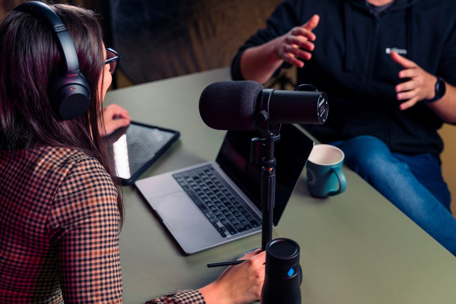 Conductor de podcast con audífonos frente a una laptop conversando con su invitado