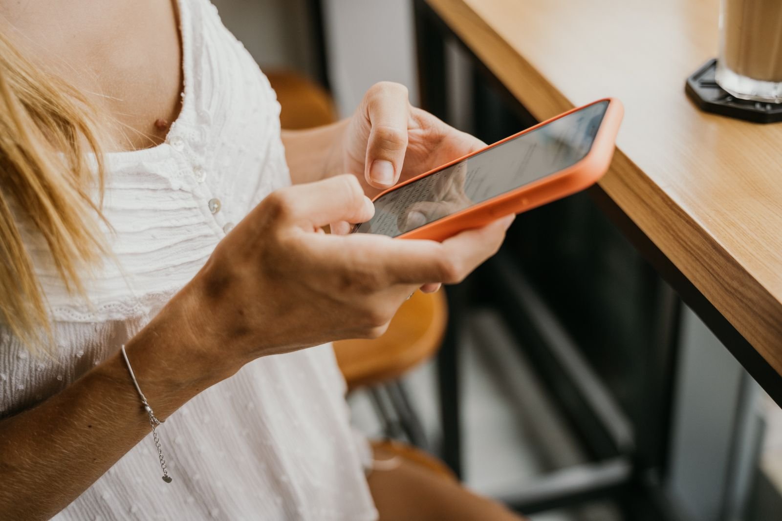 Primer plano de una mujer escribiendo en su celular sobre una mesa de madera en una cafetería