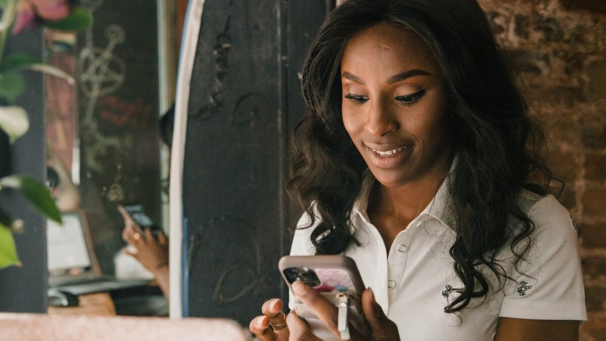 Mujer sonriente usando su celular y su laptop en una cafetería mientras trabaja