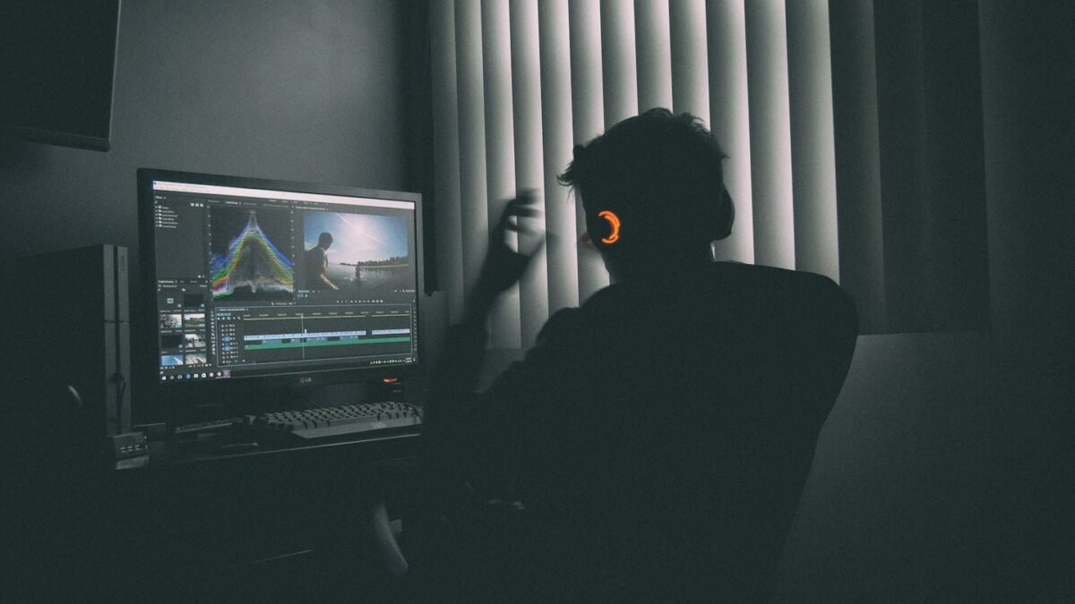 Persona en silueta con audífonos editando video en una computadora en un cuarto oscuro